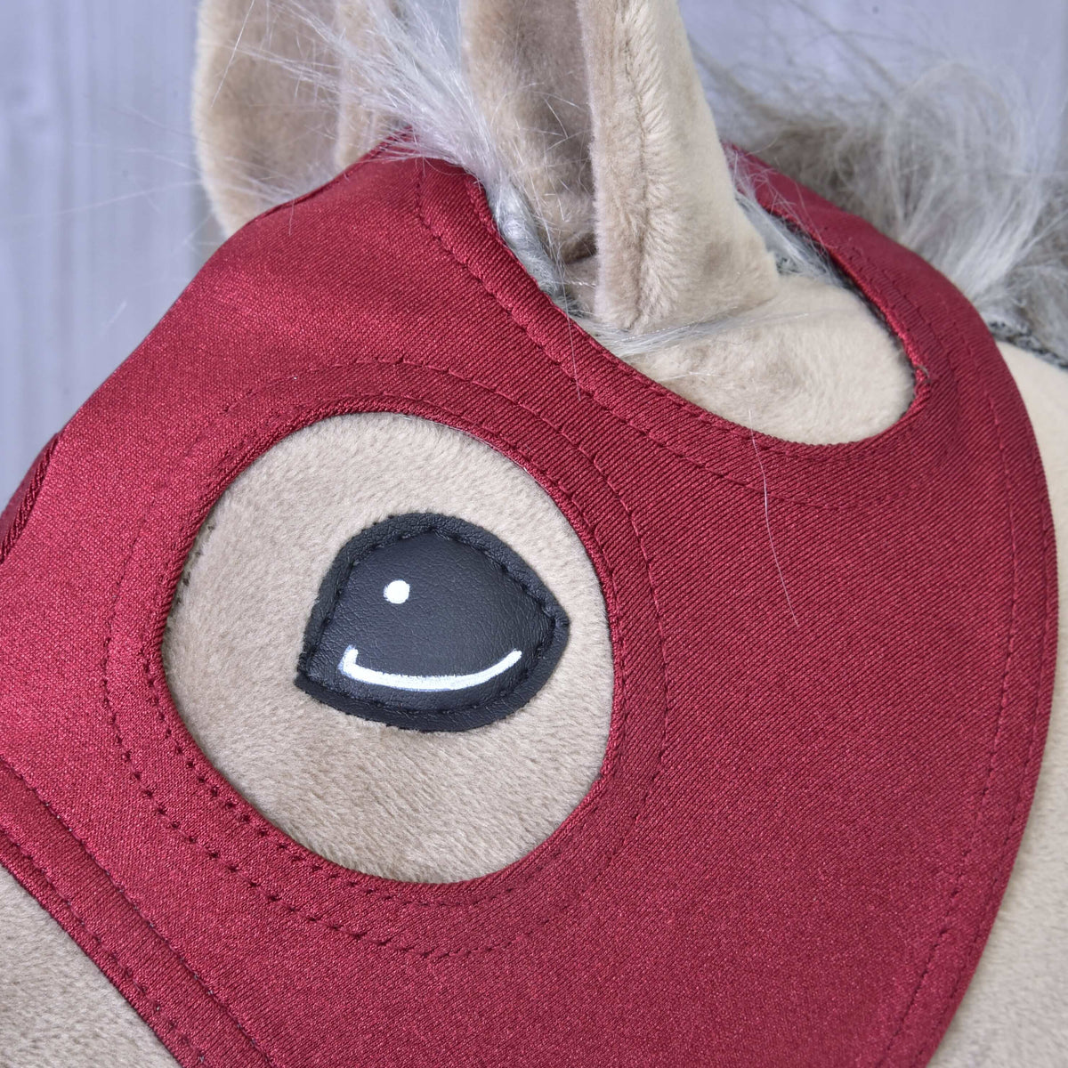 Close-up of the Hobby Horse LarDen Horse Mask without Ears Velvet, showing beige velvet fur, a red fabric bridle, stitched black and white eye, and part of the gray mane.
