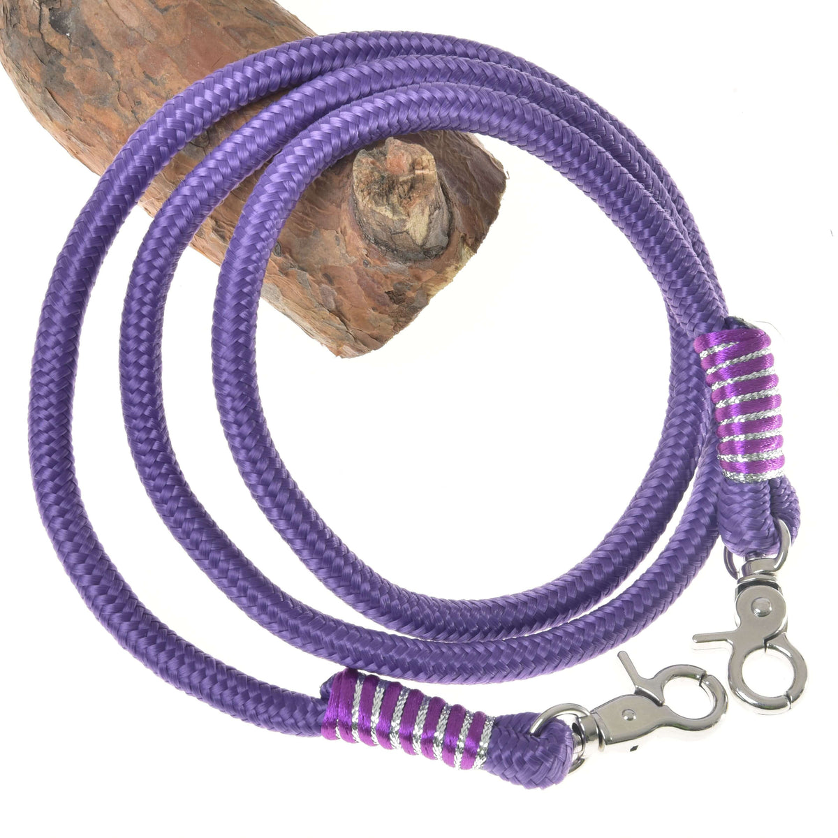 The Reins Viola by Hobby Horse LarDen features coiled purple polypropylene rope with swivel snap hooks and purple-white thread wrapping, making them ideal handmade reins for hobby horse fans—shown on a wooden log background.