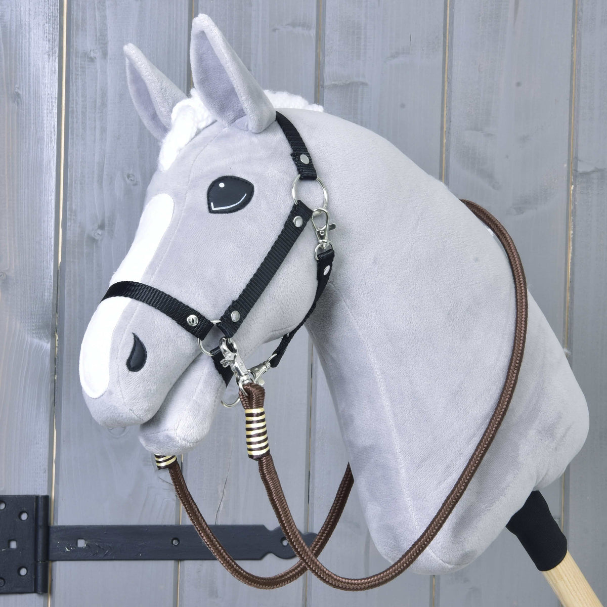 The Hobby Horse LarDen Reins Vivaldi, brown handmade polypropylene rope reins, are draped over a gray hobby horse with a white blaze and black halter on a wooden stick, set against a gray wooden background.