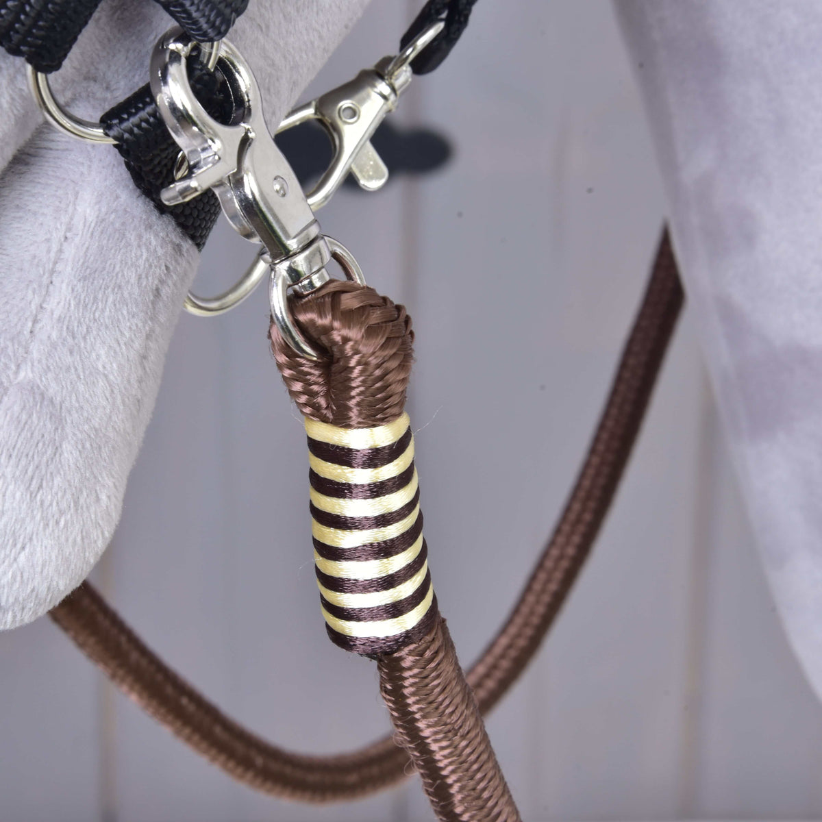 Close-up of a metal clip attaching a brown polypropylene rope with gold and black decorative wrapping to gray fabric, part of the Reins Vivaldi by Hobby Horse LarDen.