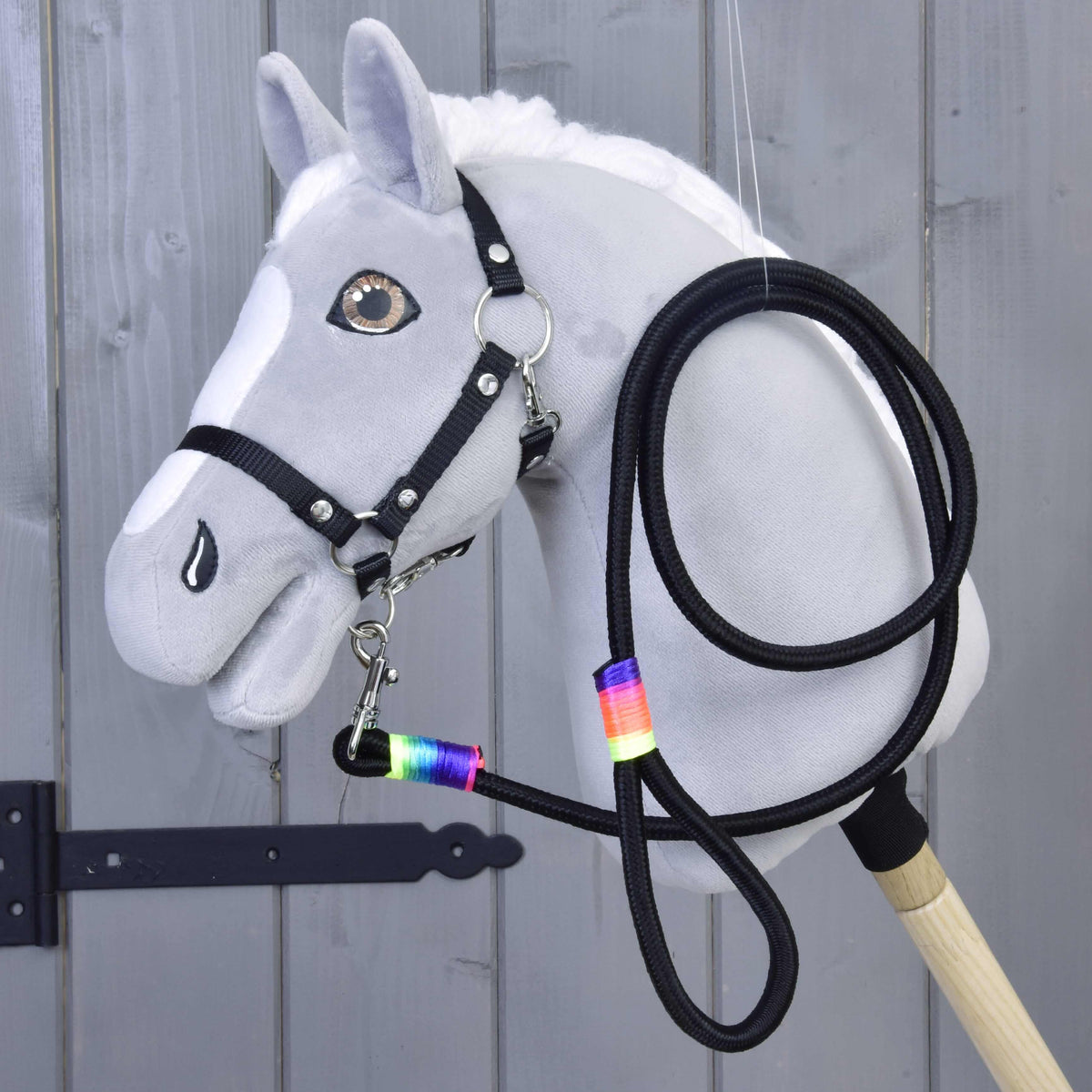 Grey plush Hobby Horse with a black halter, the black rainbow-wrapped lead rope clipped to its chin and coiled beside it