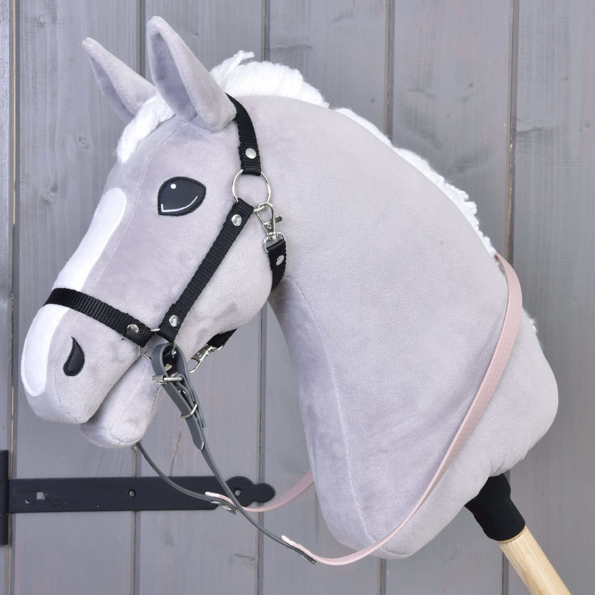 A close-up of a Hobby Horse LarDen with a light gray head, white mane, and Reins rubberized Dark Grey/Pink, attached to a cream-colored stick against a wooden background.