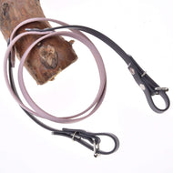 A light brown wooden branch with two Hobby Horse LarDen Reins rubberized Dark Grey/Pink looped around it, resembling leather dog leashes, against a white background.