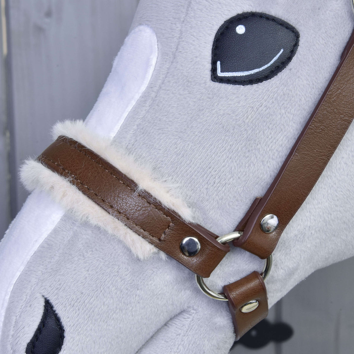 Close-up of a gray plush toy horse’s face with stitched black eyes and nose, wearing the Hobby Horse LarDen Halter with fur - leatherette Walnut, featuring fluffy cream-colored lining near the buckle.