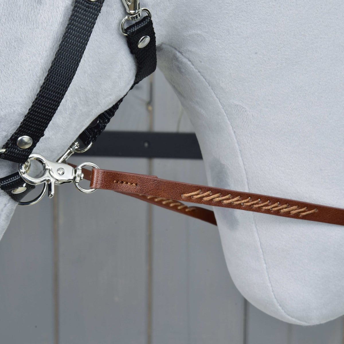 Close-up of a brown split rein with cross-stitching, its silver snap hook clipped to the ring of a black halter