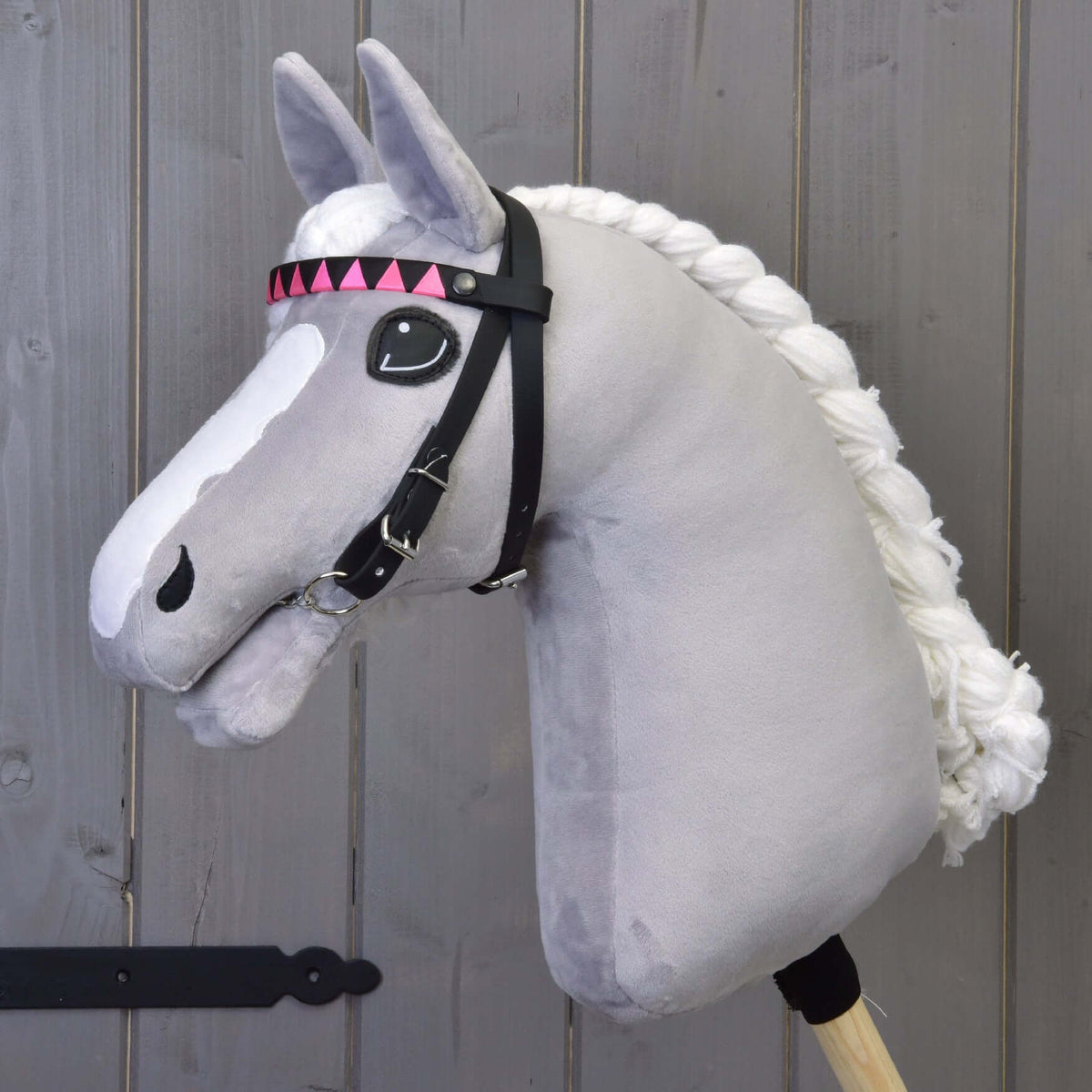 Grey plush Hobby Horse with a braided white mane wearing the black bridle with pink and black triangle browband