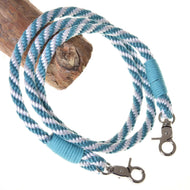 The Hobby Horse LarDen "Hobby Horse - Reins turquoise stripe" features coiled blue and white striped reins with metal clips and turquoise thread, attached to a wooden branch—ideal handmade accessories for hobby horse fans.