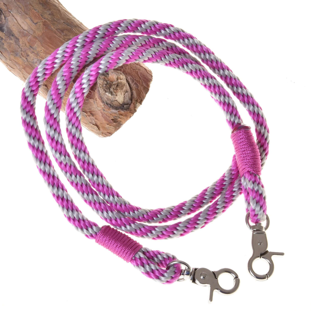 The Hobby Horse LarDen pink stripe polypropylene reins with metal clips are coiled around a wooden branch, perfect as handmade hobby horse accessories.