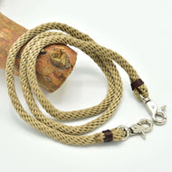 The Hobby Horse LarDen Reins Nature is a coiled, braided beige polypropylene rope with metal lobster clasps on both ends—ideal handmade reins for hobby horse enthusiasts, shown on textured wood against a white background.