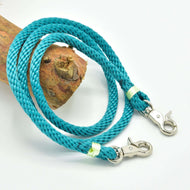 The Reins Turquoise by Hobby Horse LarDen is a handmade turquoise braided rope with silver clasps at both ends, ideal for hobby horse reins, shown coiled on wood against a white background.